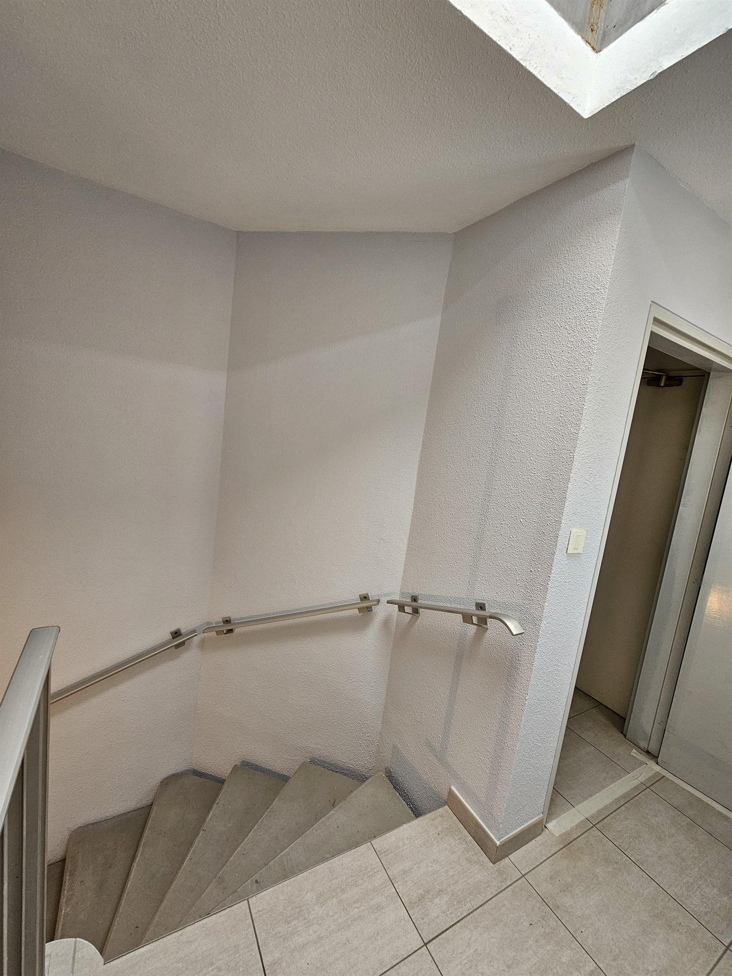 Cage d'escalier de copropriété terminée, murs clairs, main courante et palier carrelé