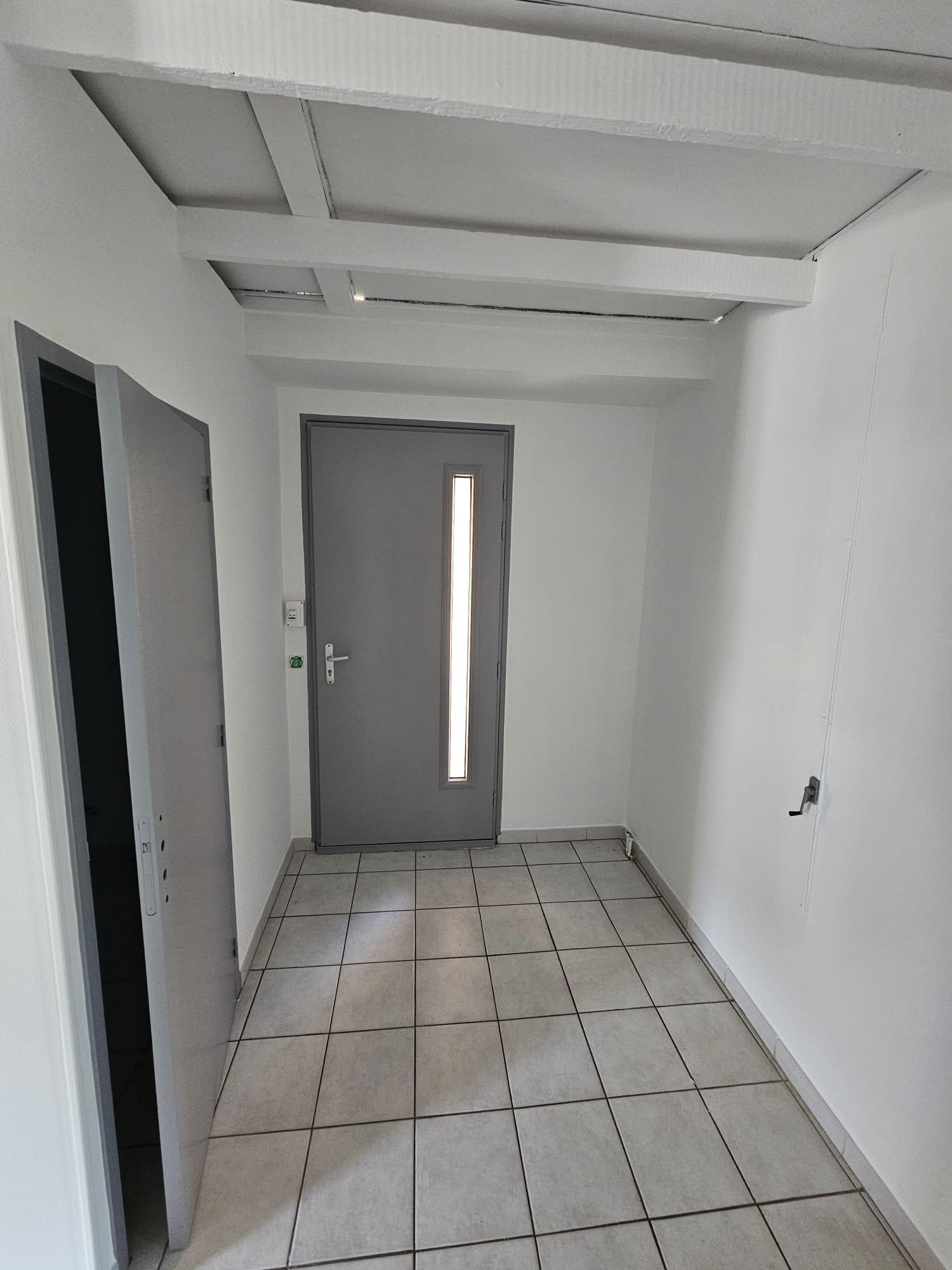 Entrée sous combles avec poutres apparentes peintes en blanc et porte palière grise