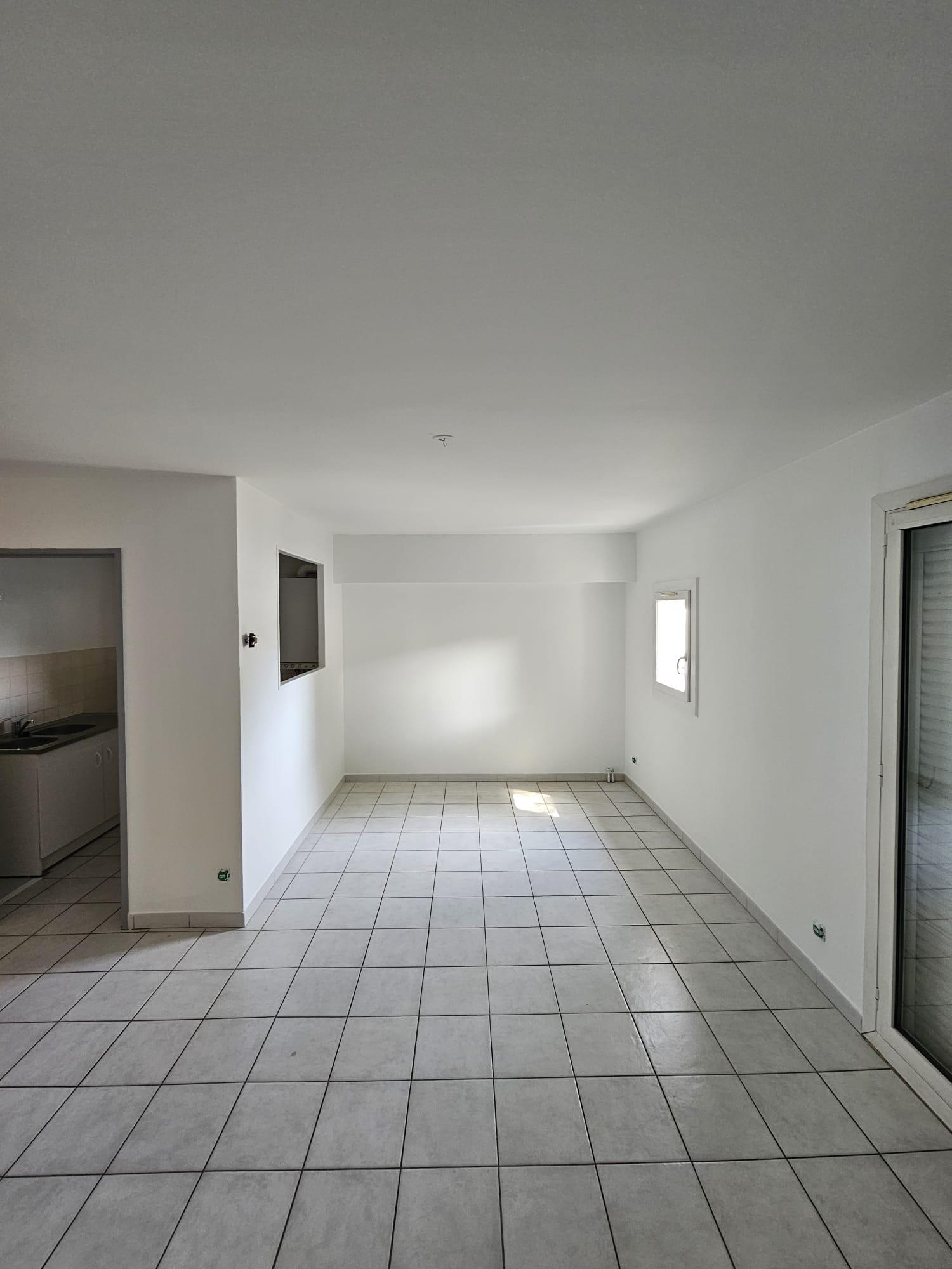 Séjour d'un appartement vide à Perpignan, murs et plafond blancs, ouverture sur la cuisine, carrelage beige