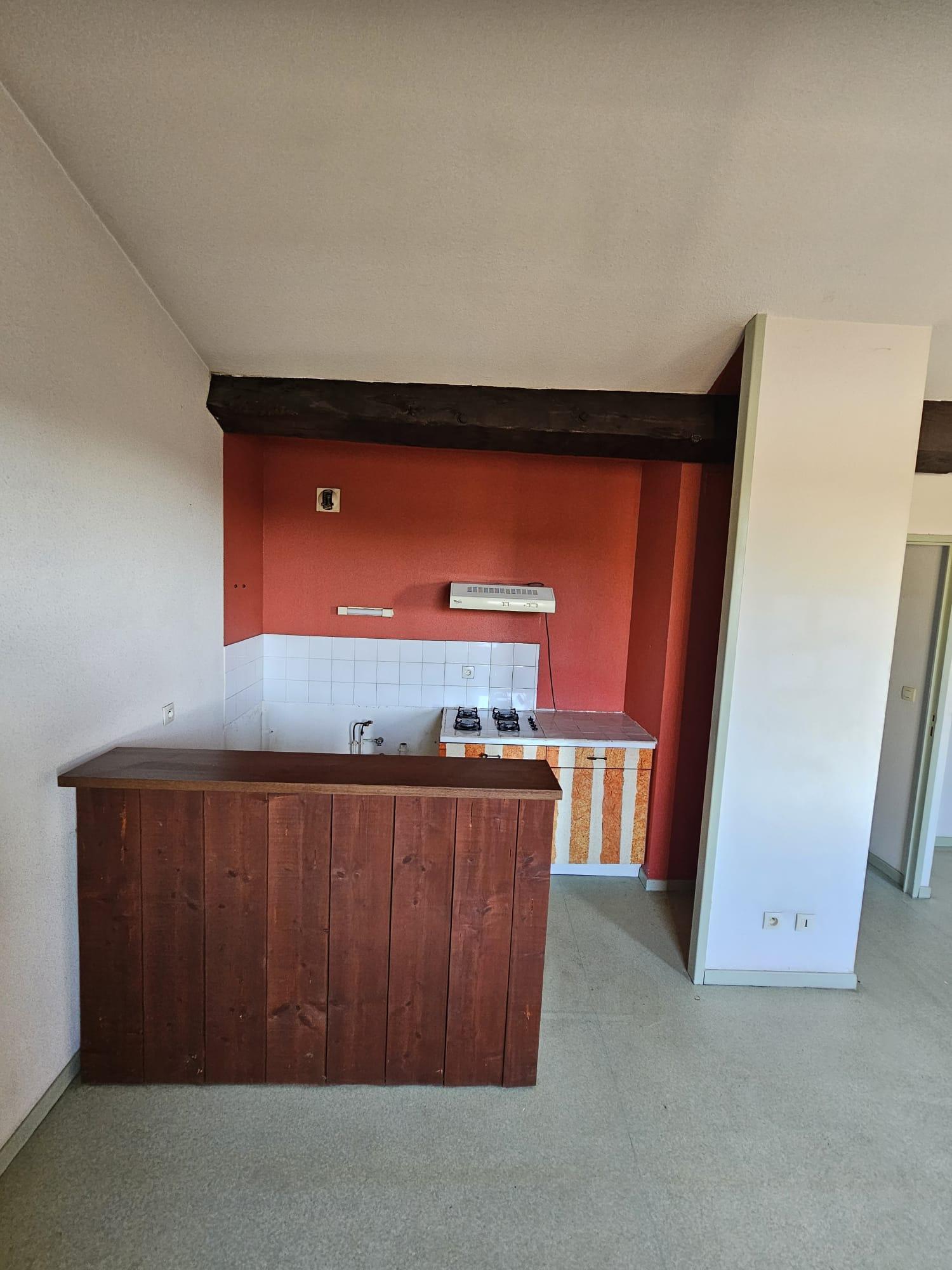 Cuisine d'une maison de village avant travaux, mur rouge, bar en bois, poutre apparente