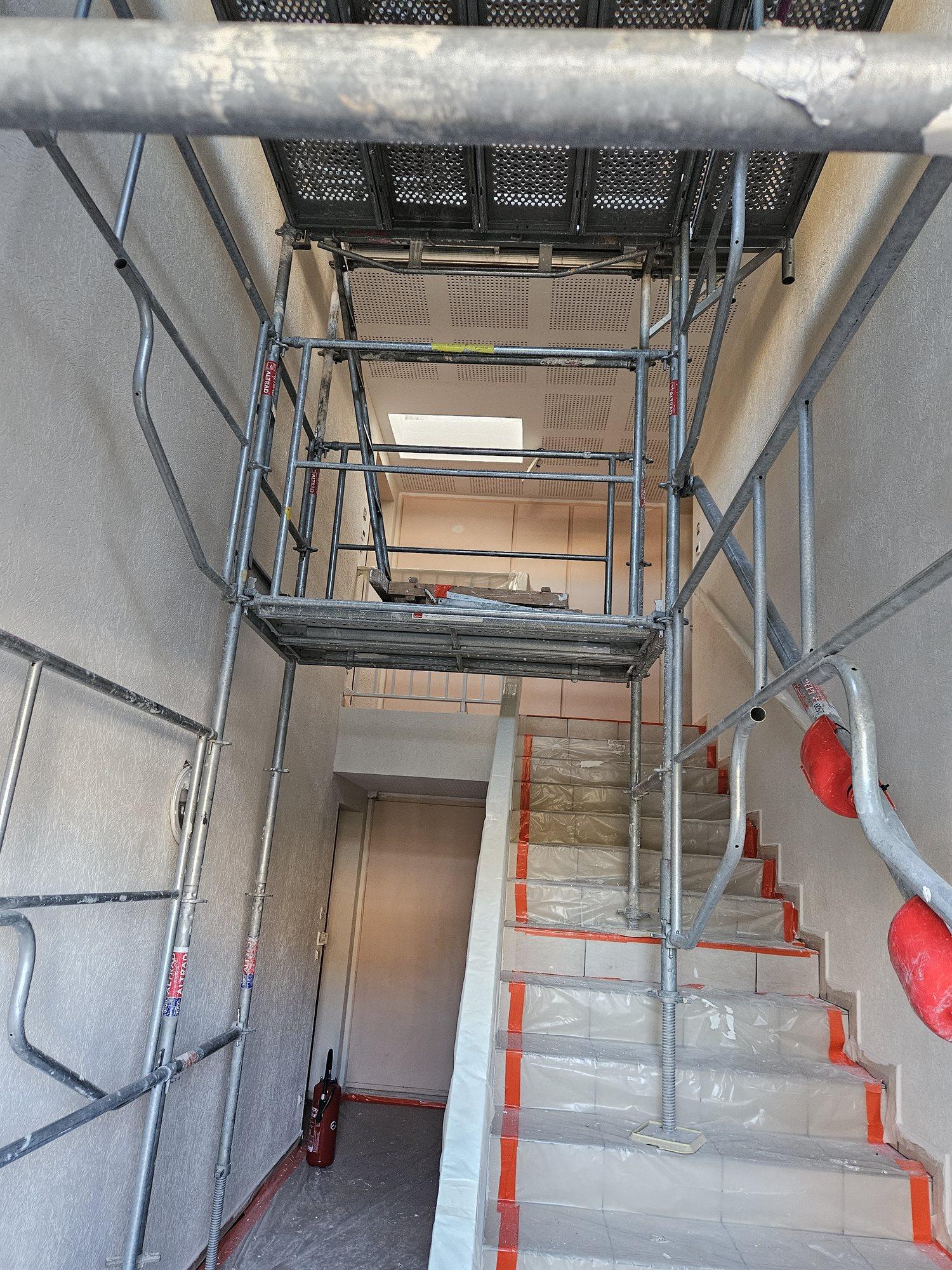 Cage d'escalier de copropriété en travaux, échafaudage roulant monté dans la trémie et marches protégées