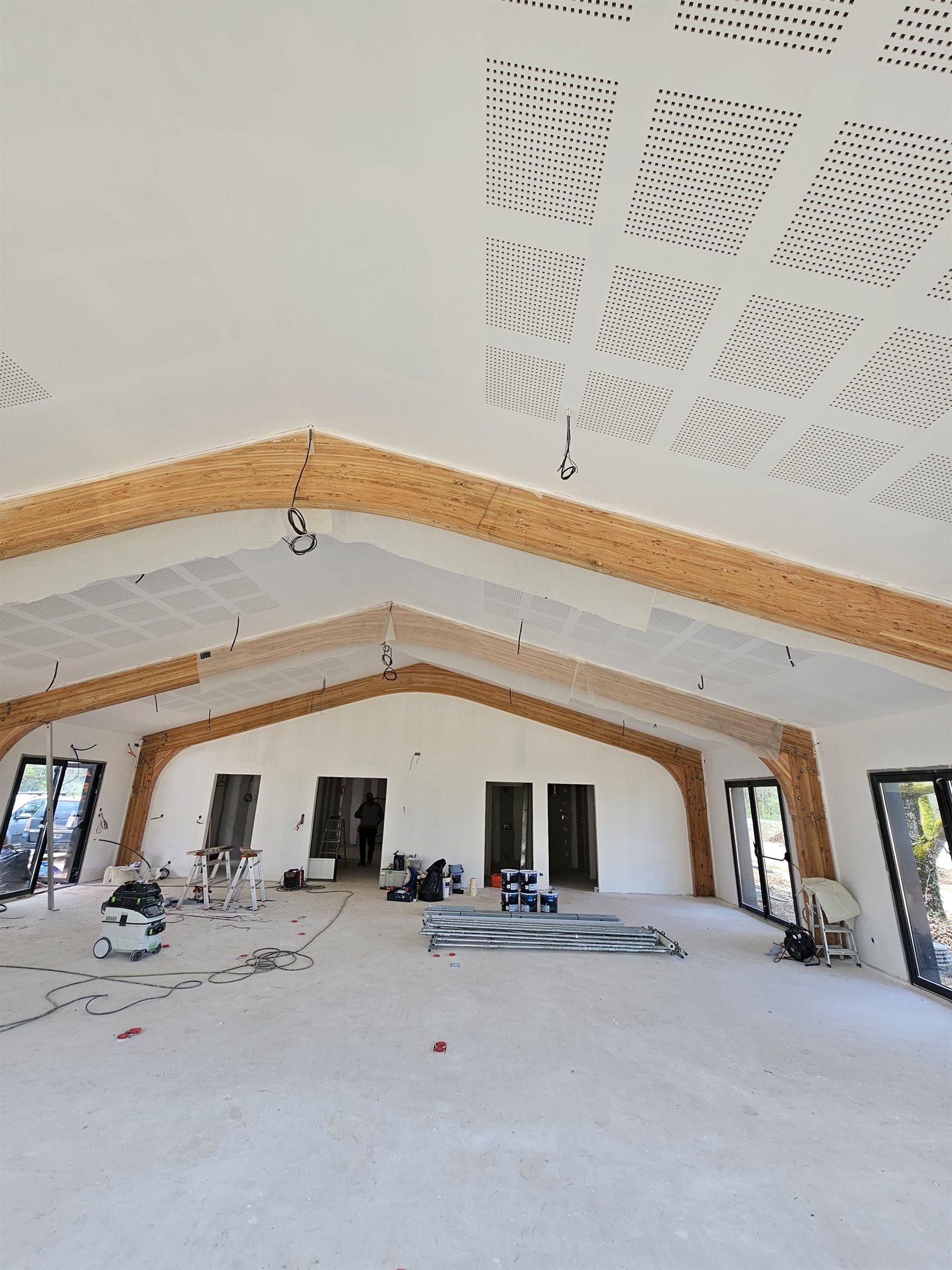 Grand volume neuf avec charpente en lamellé-collé apparente et plafond acoustique perforé, en cours de peinture