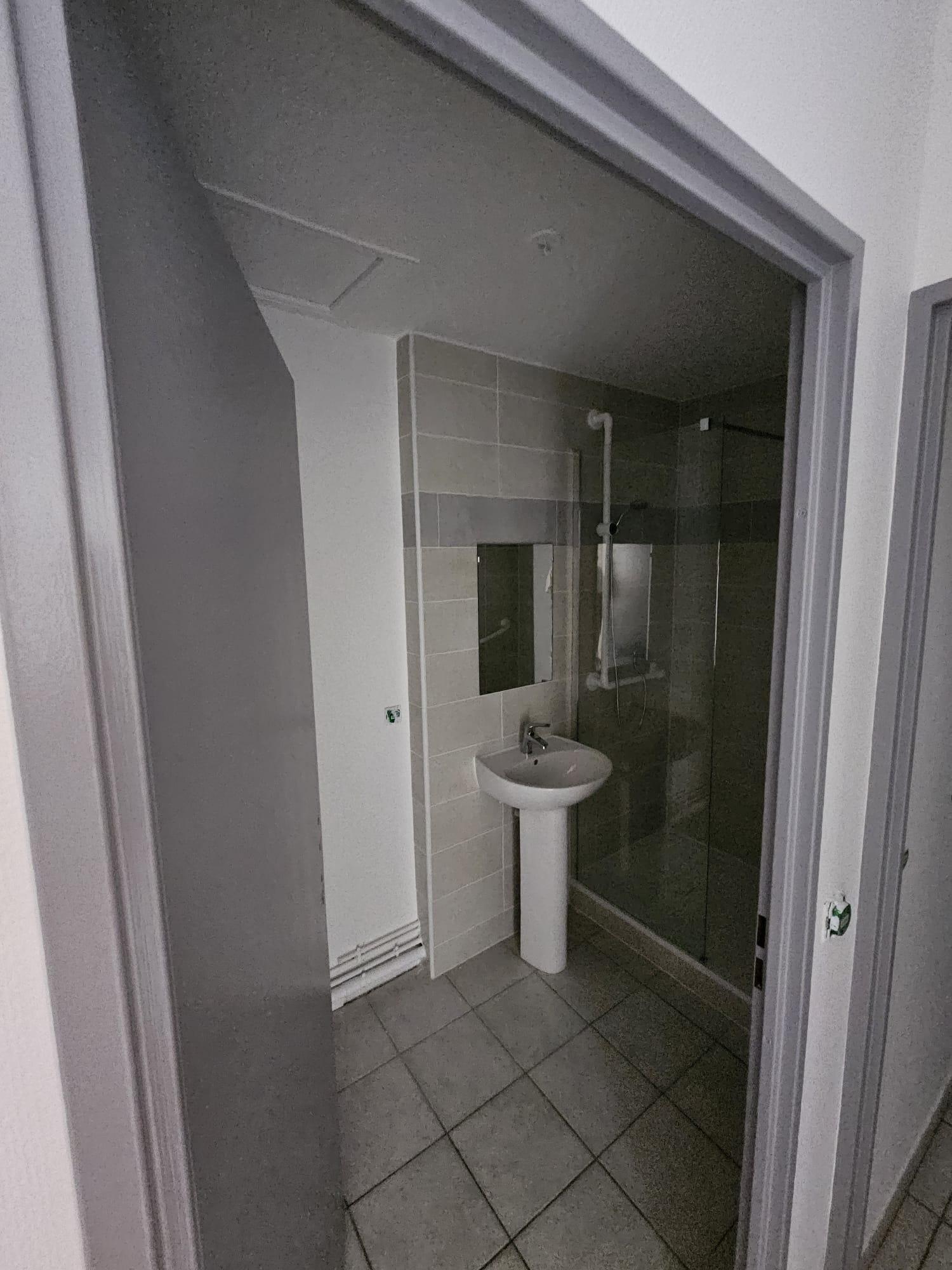 Salle d'eau avec douche et lavabo, murs peints en blanc au-dessus de la faïence